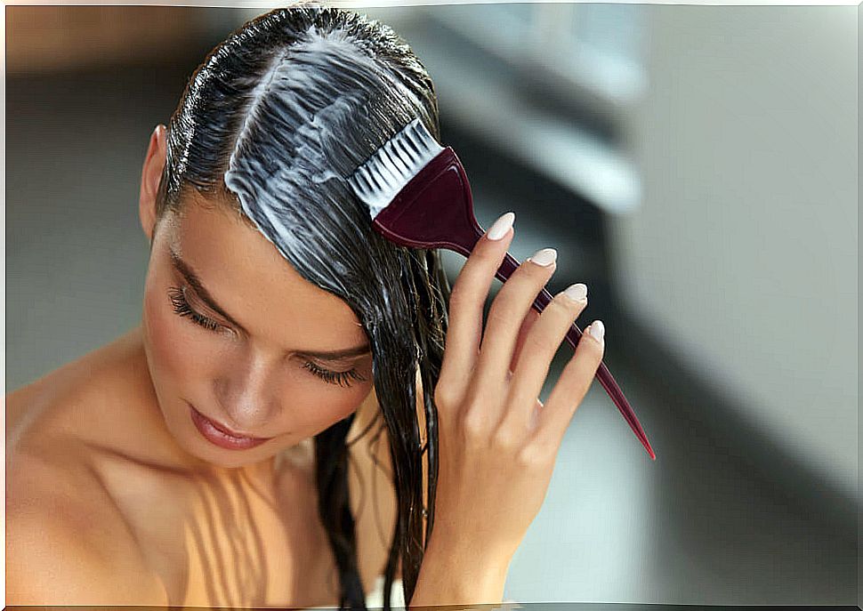 Woman applying a mask to her hair with the help of a comb in the shape of a brush.